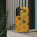 Phone case with orange and brown paw prints design, medium size, displayed upright on wooden surface