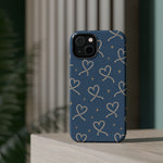 Lasso Hearts – Blue Western Heart MagSafe Phone Case, glossy diagonal dual-camera model, rear view on a tabletop