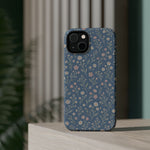 Denim Wildflowers MagSafe Phone Case, glossy diagonal dual-camera model, rear view on a tabletop