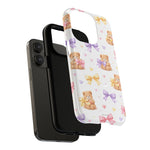 Black smartphone with two protective cases, one solid black and one white with teddy bears and colorful bows pattern, showing case size variant