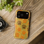 Yellow and green iPhone case with orange and brown paw prints, variant size shown on table