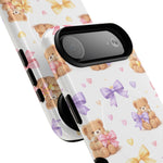 Close-up of two phone cases with cute teddy bear, bow, and heart patterns, showing different sizes