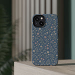 Denim Wildflowers MagSafe Phone Case, glossy diagonal dual-camera model, rear view on a tabletop