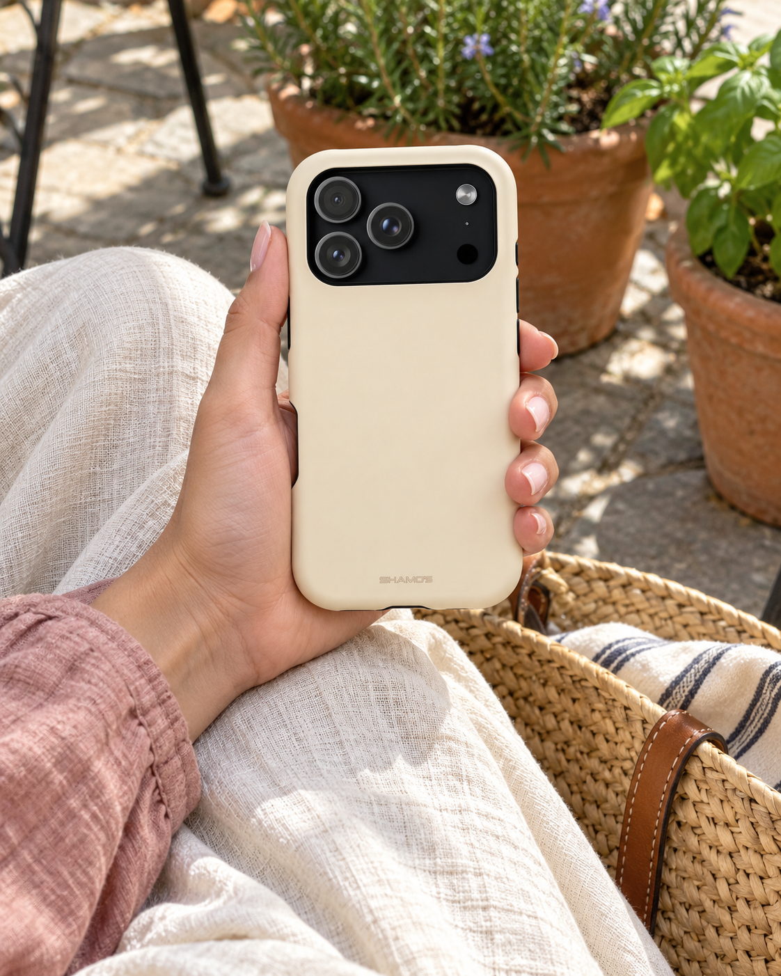 Buttercream phone case held above a woven bag in a sunny courtyard