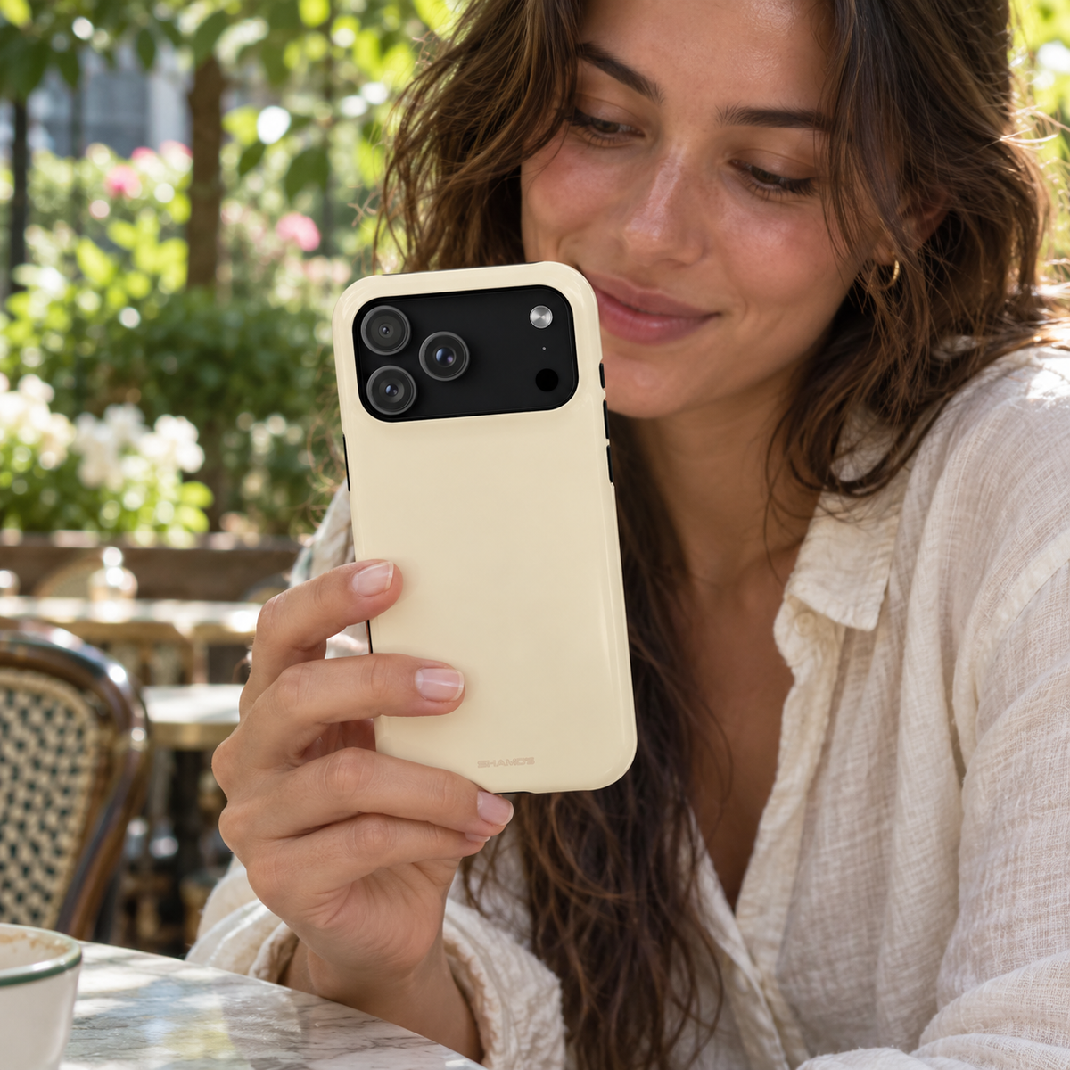 Woman holding a buttercream phone case while seated at a leafy garden café