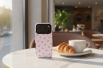 Cherry-pattern pink case standing on a cafe table beside coffee and a croissant #iphone-18-pro