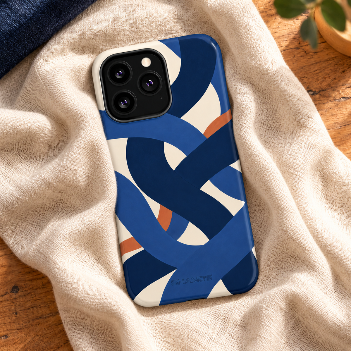 Indigo Loom glossy case with square triple-camera opening on ivory linen beside a wooden desk