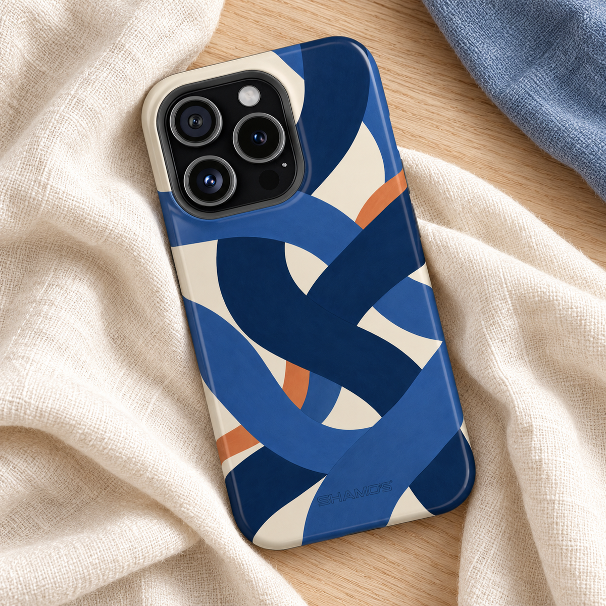 Indigo Loom glossy case with square triple-camera opening resting on ivory linen and oak