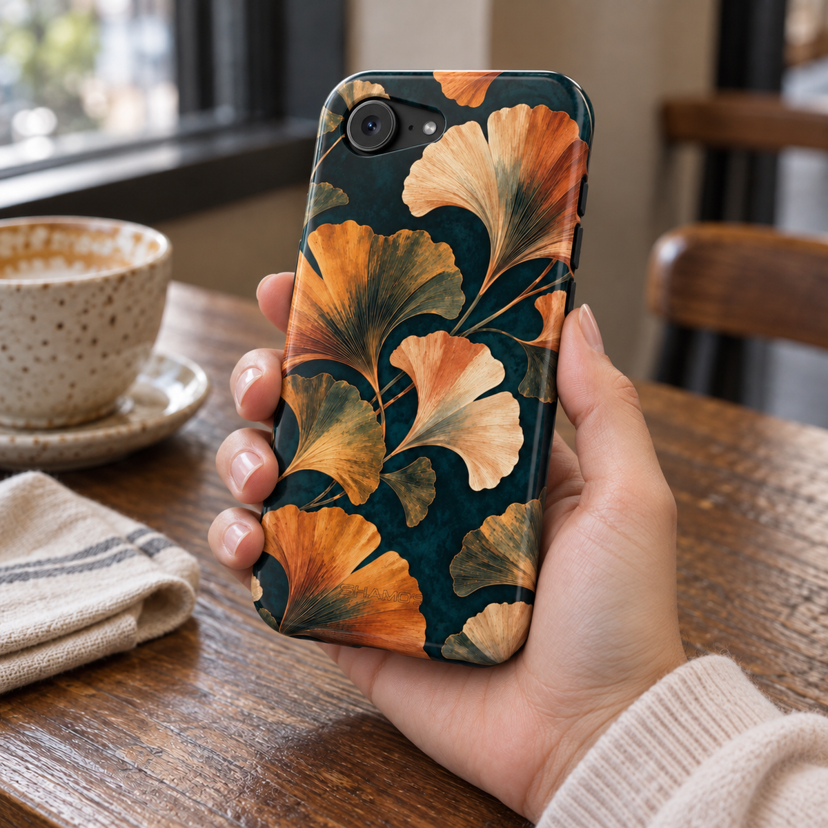 Adult woman holding the Nocturne Ginkgo iPhone 16e case at a cafe #iphone-16e