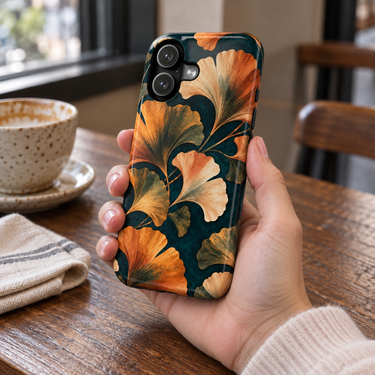 Adult woman holding the Nocturne Ginkgo iPhone 17 case at a cafe #iphone-17