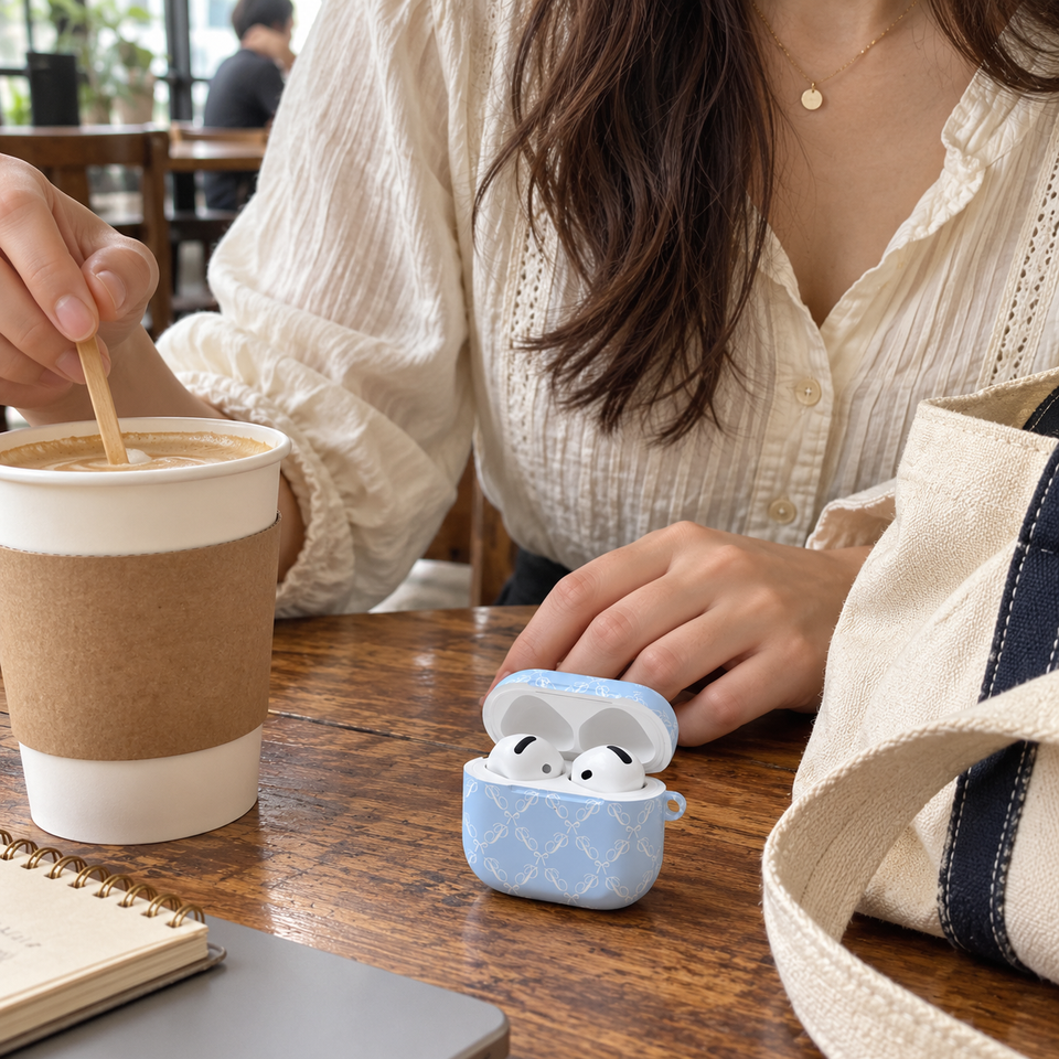 Blue bow earbud case beside a woman’s coffee and canvas tote at a café