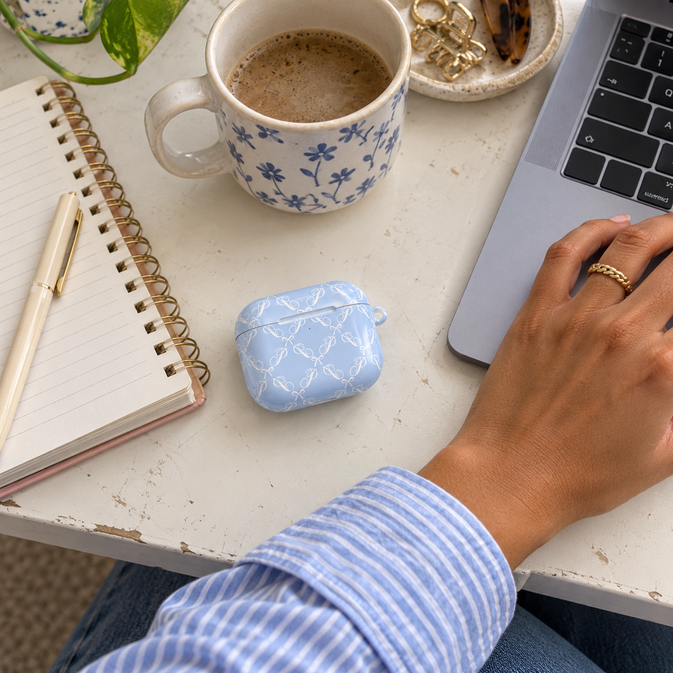 Blue bow earbud case beside a notebook while a woman works on her laptop