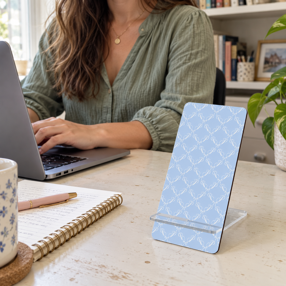 Blue bow phone stand beside a laptop in a woman’s home workspace