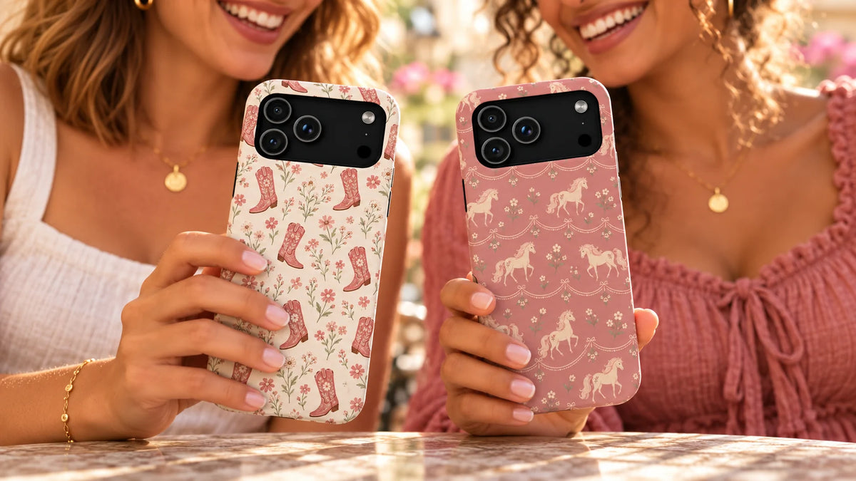 Close-up of Floral Boots and Rose Ponies phone cases held by two smiling friends at a sunny café.